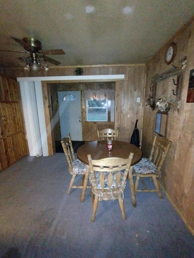 carpeted dining space with ceiling fan and wood walls