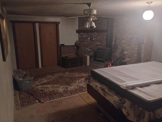 bedroom with a textured ceiling, a wood stove, and ceiling fan