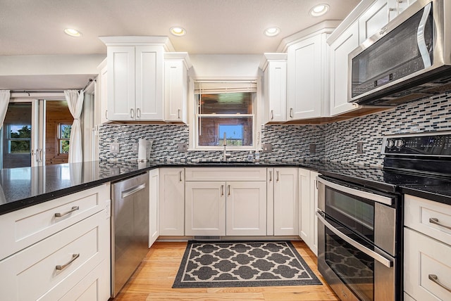 kitchen with white cabinets, sink, dark stone counters, appliances with stainless steel finishes, and light wood-type flooring