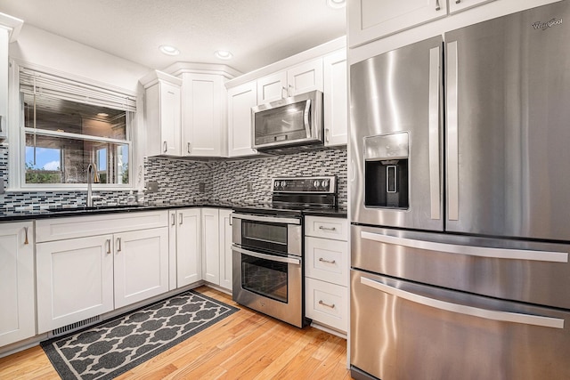 kitchen featuring sink, backsplash, white cabinetry, appliances with stainless steel finishes, and light wood-type flooring