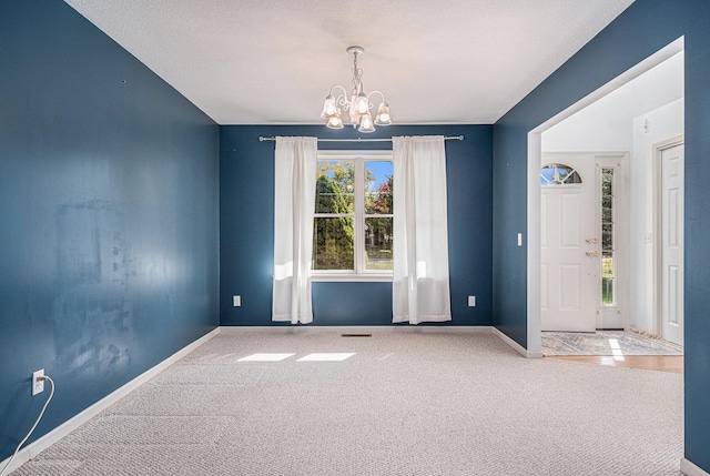 empty room with a textured ceiling, a notable chandelier, and carpet flooring