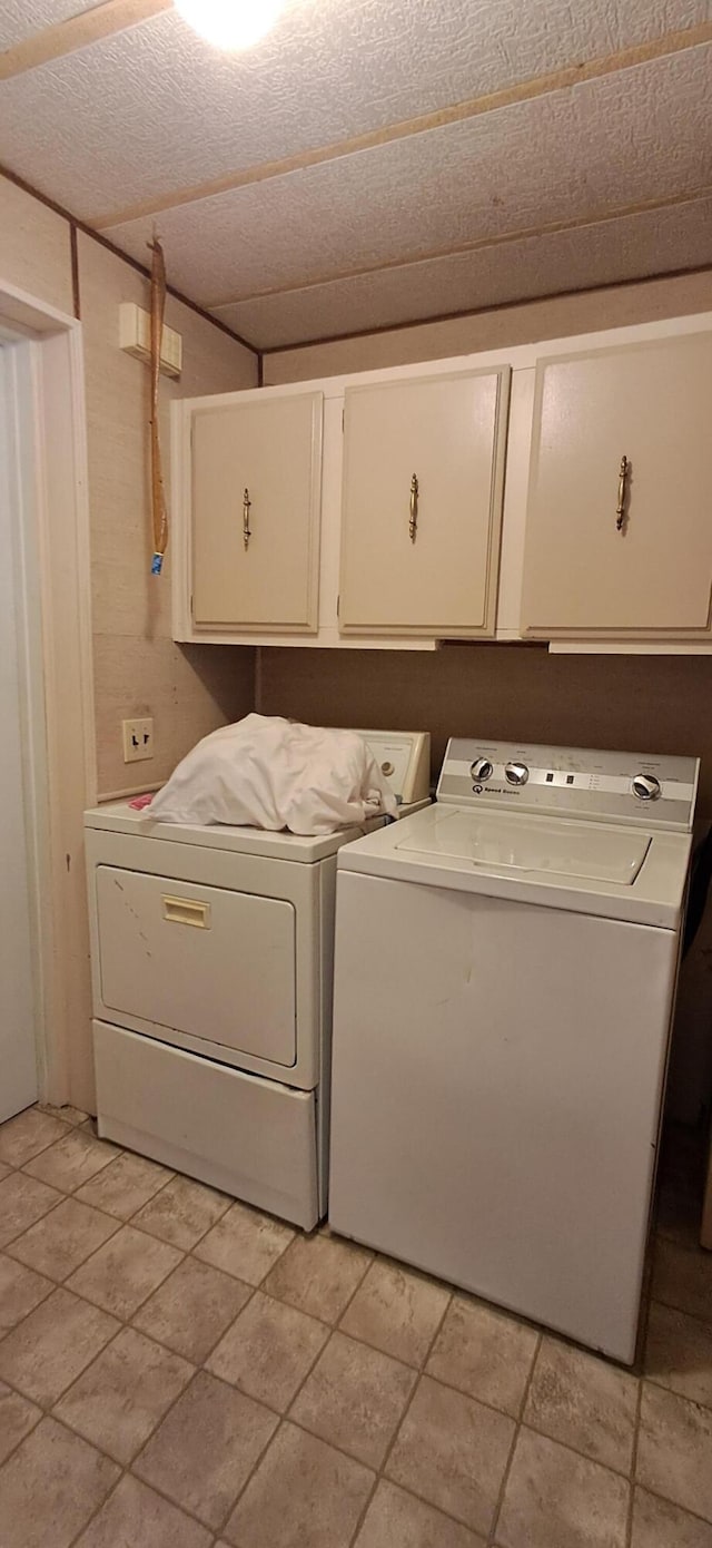 clothes washing area featuring cabinets, a textured ceiling, light tile patterned floors, and washing machine and dryer