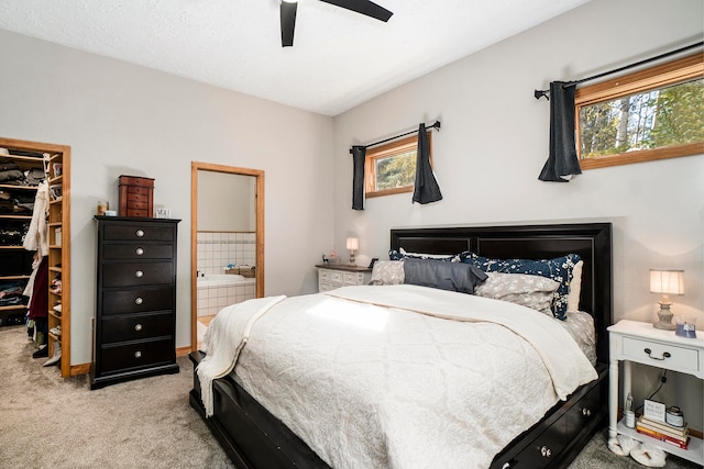 carpeted bedroom featuring ensuite bath, multiple windows, ceiling fan, and a walk in closet