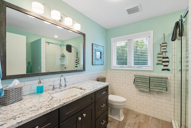 bathroom with vanity, hardwood / wood-style flooring, tile walls, toilet, and a shower with shower door