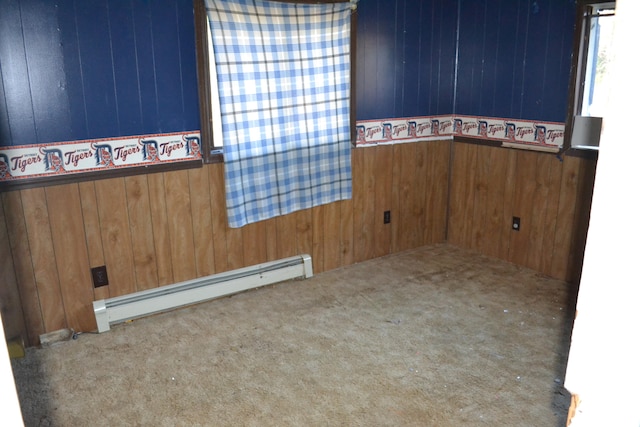 carpeted empty room featuring wood walls and a baseboard heating unit