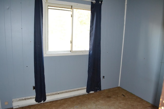 spare room featuring wooden walls, carpet flooring, and a baseboard heating unit