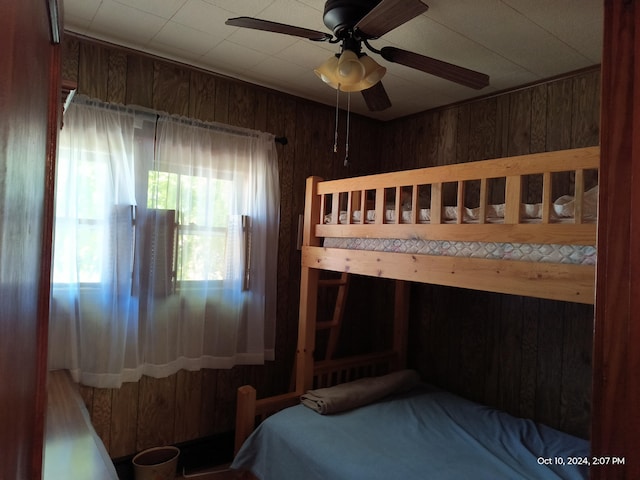 bedroom featuring ceiling fan and wood walls