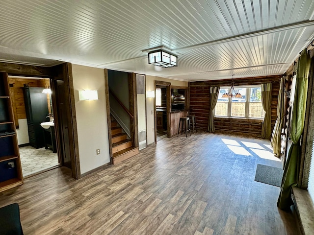 unfurnished living room featuring a notable chandelier, wood walls, and wood-type flooring