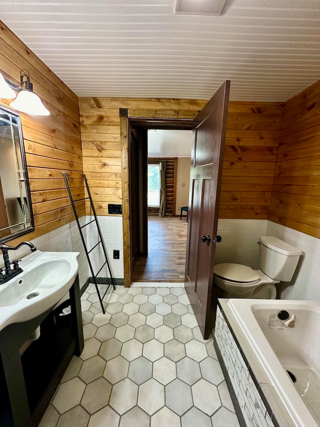 bathroom featuring toilet, wood walls, a tub to relax in, and vanity