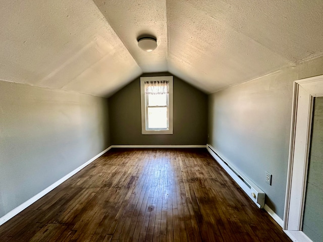 additional living space featuring a baseboard radiator, vaulted ceiling, a textured ceiling, and dark hardwood / wood-style flooring