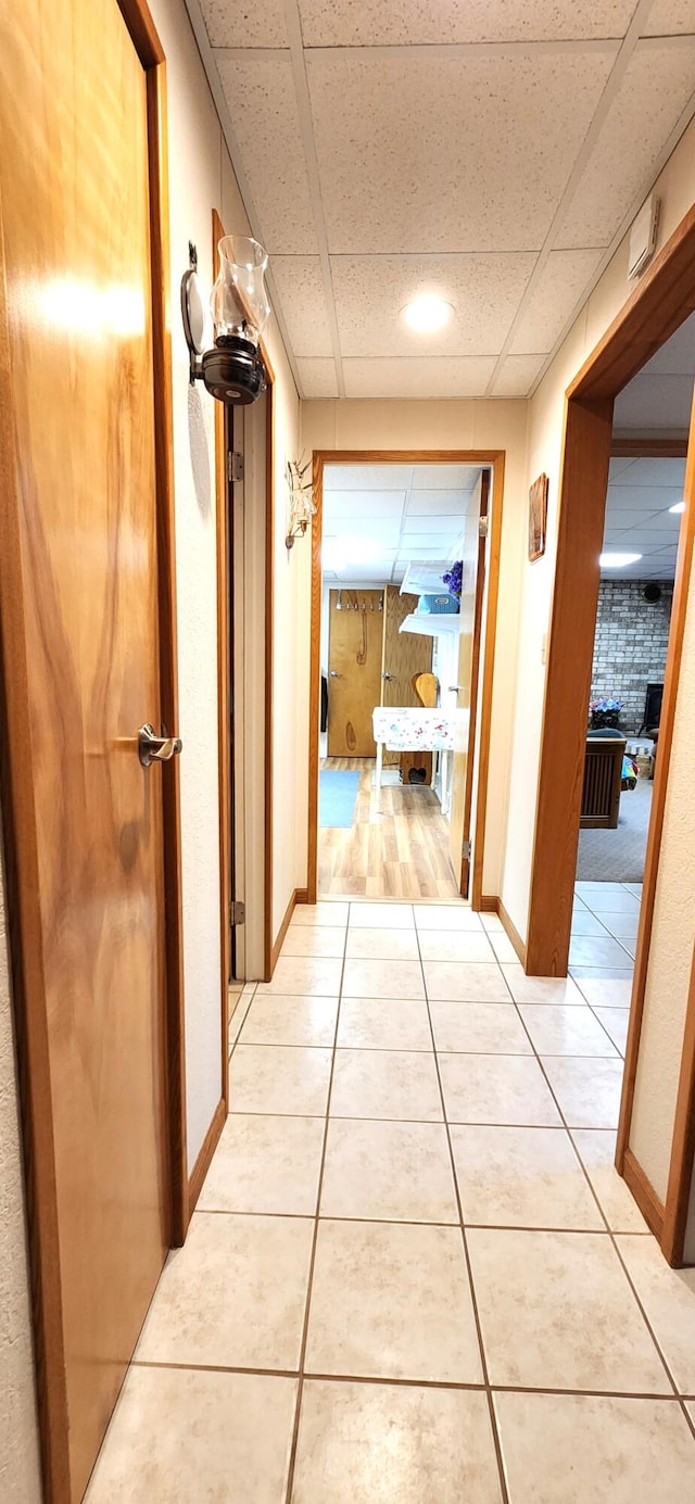 hallway featuring a drop ceiling and light tile patterned floors