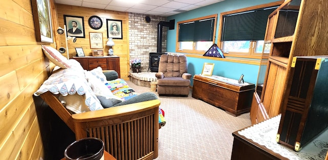 living area with wooden walls, a drop ceiling, carpet flooring, and a wood stove