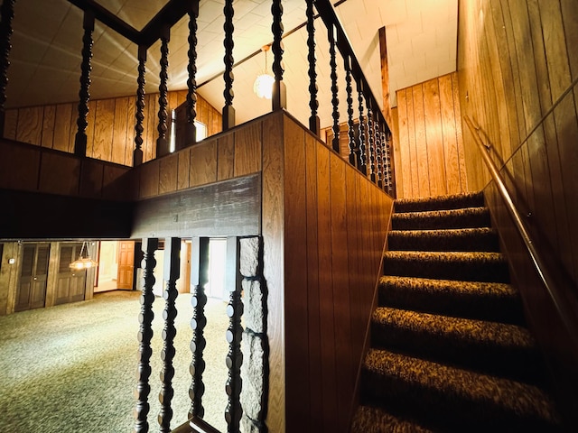 stairs with high vaulted ceiling, wood walls, and carpet