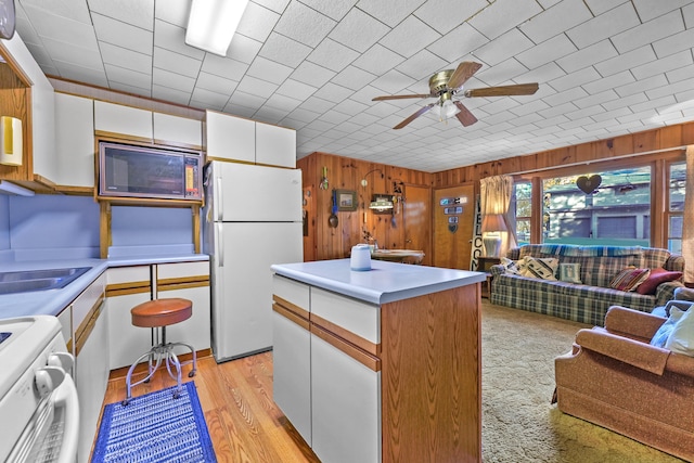 kitchen featuring white cabinets, wood walls, light hardwood / wood-style floors, a center island, and white appliances