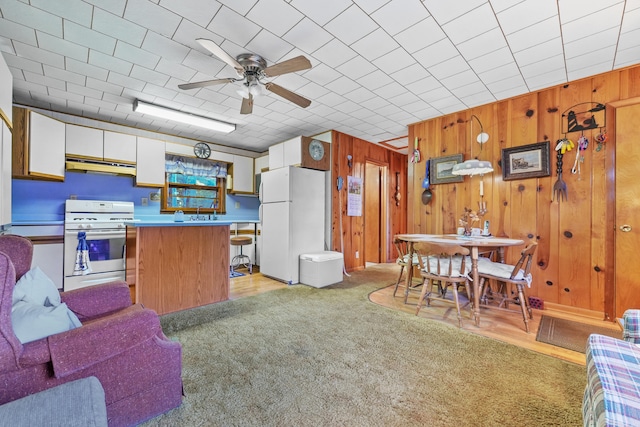 kitchen featuring white appliances, ceiling fan, wood walls, and white cabinets