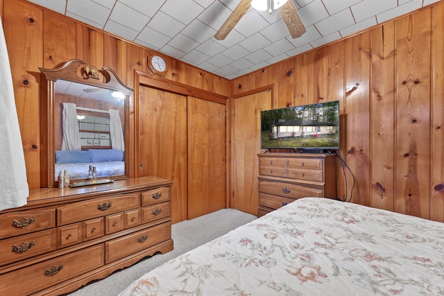 carpeted bedroom featuring a closet, wood walls, and ceiling fan