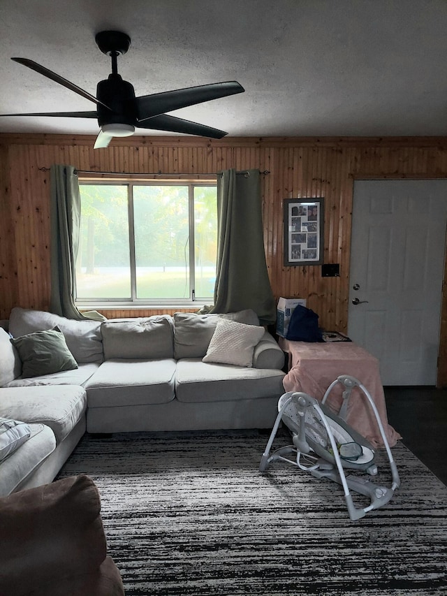 living room with ceiling fan, a textured ceiling, and wooden walls