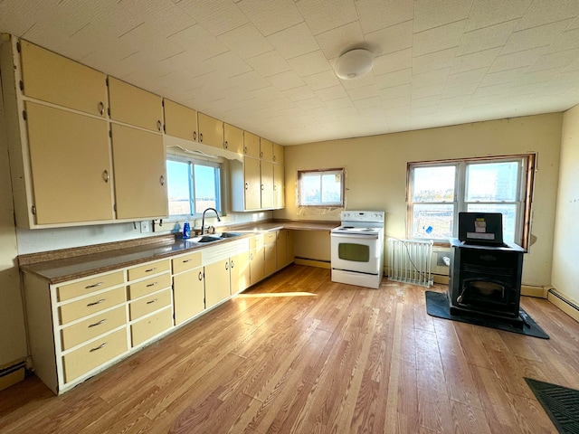 kitchen featuring cream cabinetry, light hardwood / wood-style flooring, a wood stove, sink, and electric range