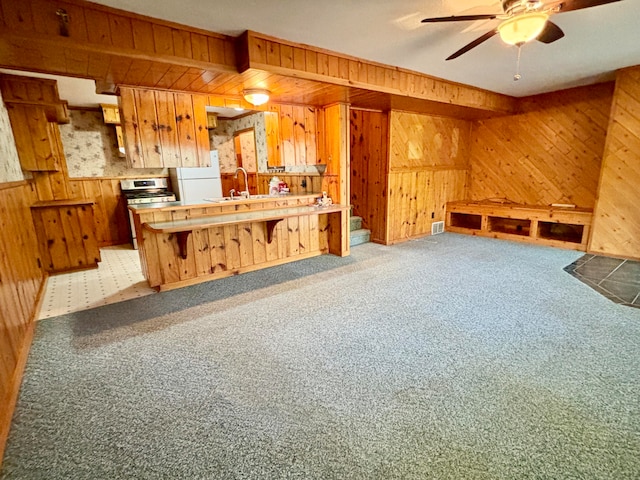 kitchen with ceiling fan, carpet flooring, sink, wooden walls, and white refrigerator