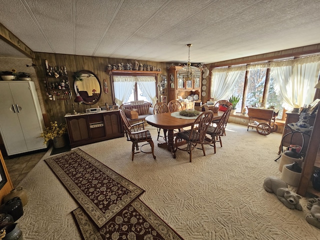 carpeted dining area featuring a textured ceiling, a chandelier, and wooden walls