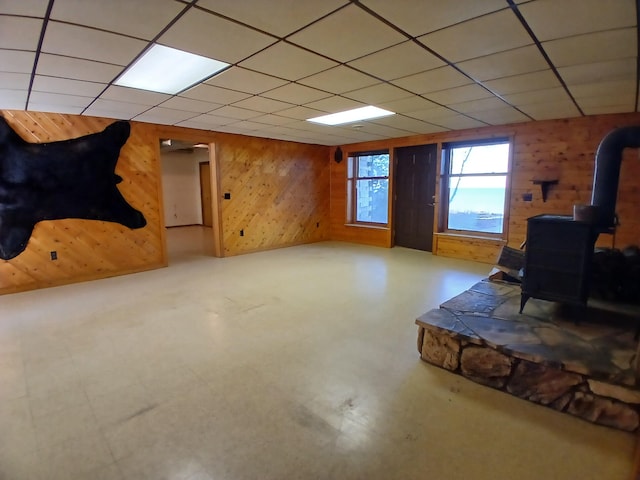 basement featuring wood walls, a paneled ceiling, and a wood stove