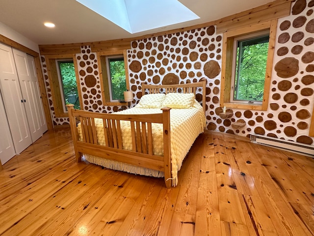 unfurnished bedroom with a closet, light hardwood / wood-style floors, a skylight, and wooden walls