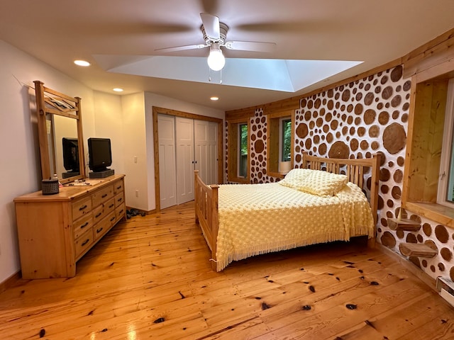 bedroom featuring a closet, a baseboard heating unit, light wood-type flooring, a skylight, and ceiling fan