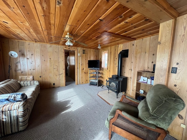 carpeted living room with wooden walls, ceiling fan, a wood stove, and wooden ceiling