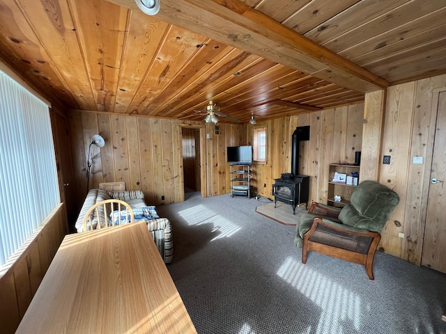 living room featuring wooden ceiling, ceiling fan, a wood stove, and wooden walls