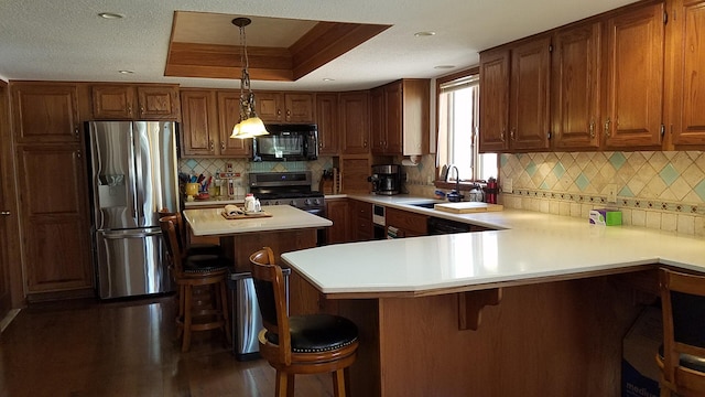 kitchen with brown cabinetry, a raised ceiling, stainless steel appliances, light countertops, and a sink