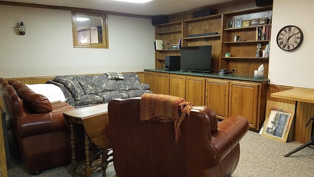 living area featuring light carpet, wood walls, a wainscoted wall, and a paneled ceiling