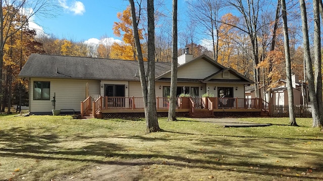 rear view of property with a deck, roof with shingles, a lawn, and a chimney