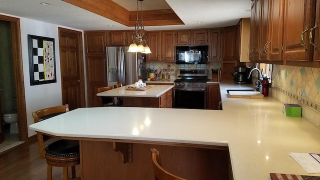 kitchen featuring a sink, light countertops, appliances with stainless steel finishes, a tray ceiling, and tasteful backsplash