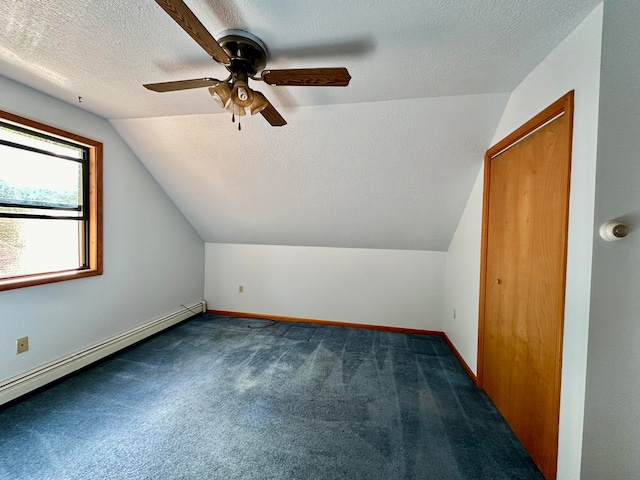 additional living space with baseboard heating, dark colored carpet, lofted ceiling, and a textured ceiling