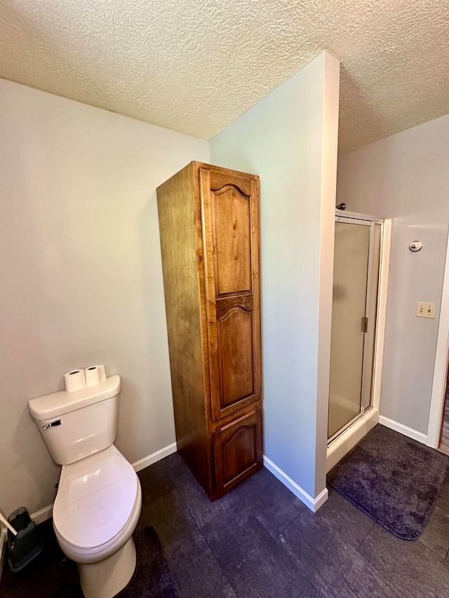 bathroom with a textured ceiling, toilet, and a shower with door