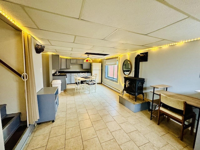 interior space with light tile patterned floors, a paneled ceiling, stairs, freestanding refrigerator, and a wood stove