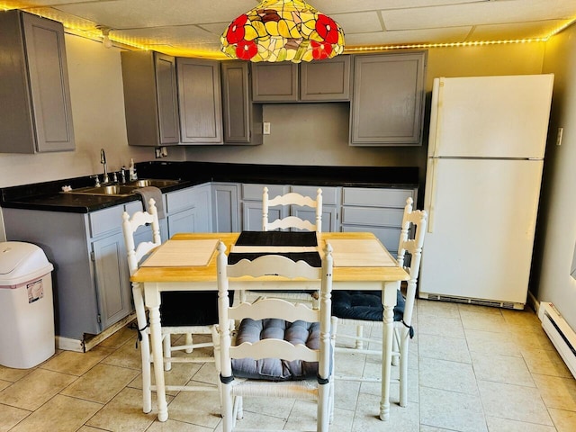 kitchen featuring dark countertops, baseboard heating, freestanding refrigerator, light tile patterned flooring, and a sink