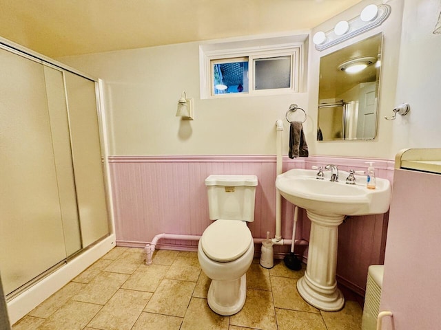 bathroom with toilet, a shower stall, tile patterned flooring, and wainscoting