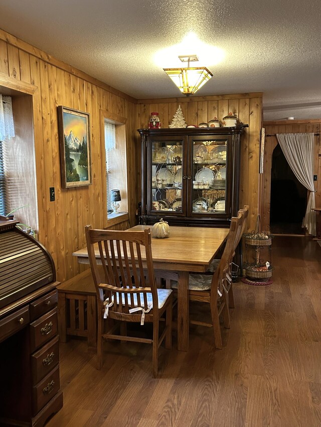 dining room featuring wood walls, a textured ceiling, and dark hardwood / wood-style floors