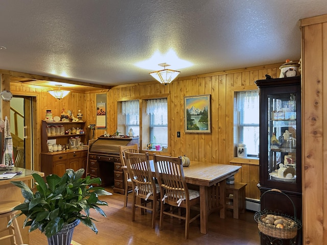 dining area featuring wooden walls, a textured ceiling, and hardwood / wood-style flooring