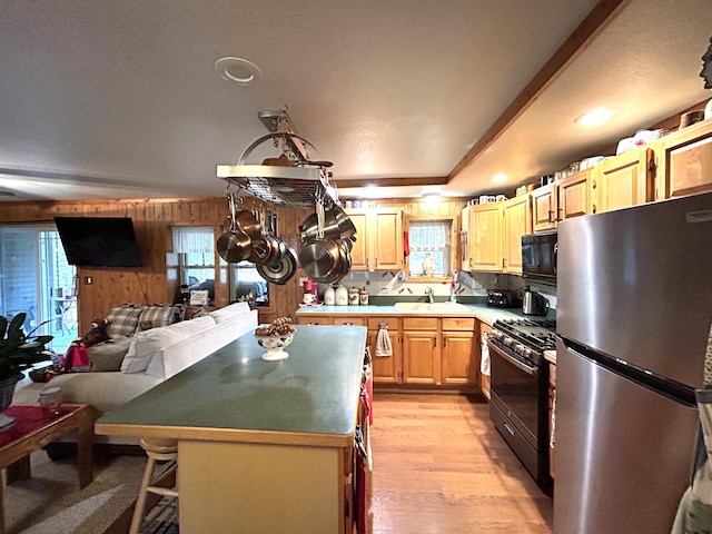 kitchen with black appliances, a kitchen bar, light hardwood / wood-style flooring, a center island, and wooden walls