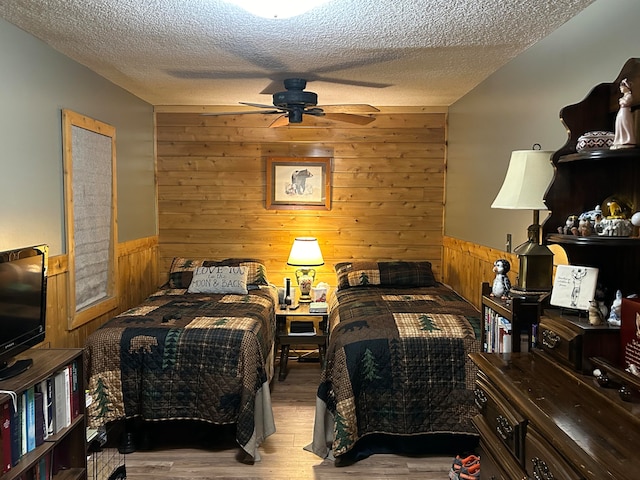 bedroom featuring wood walls, light hardwood / wood-style floors, ceiling fan, and a textured ceiling