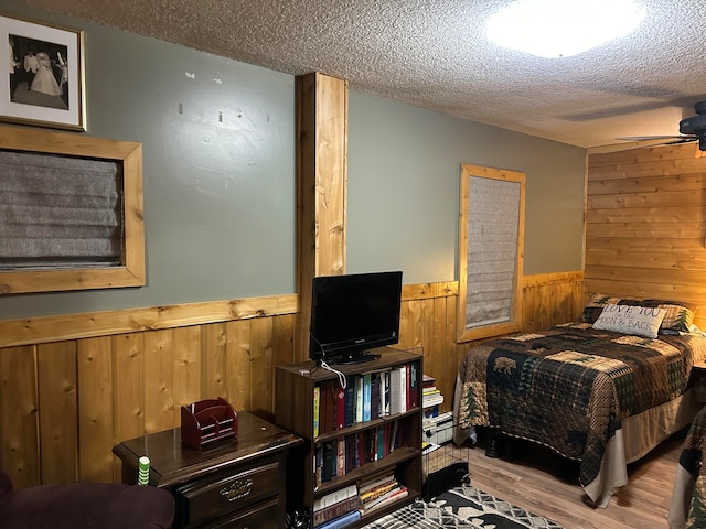 bedroom with wood walls, a textured ceiling, and light hardwood / wood-style floors