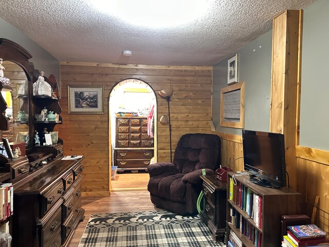 sitting room with a textured ceiling, wooden walls, and light hardwood / wood-style flooring