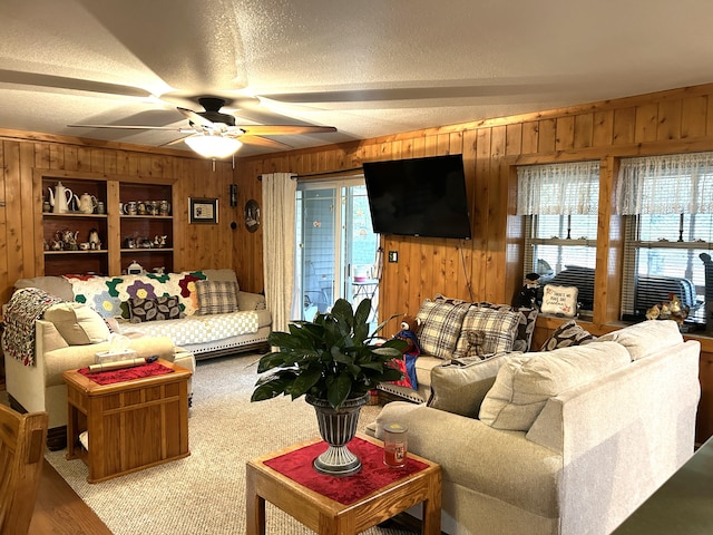 carpeted living room with wood walls, ceiling fan, plenty of natural light, and a textured ceiling