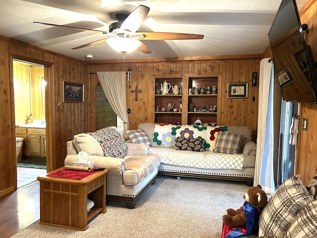 living room featuring a textured ceiling, light hardwood / wood-style floors, wooden walls, and ceiling fan