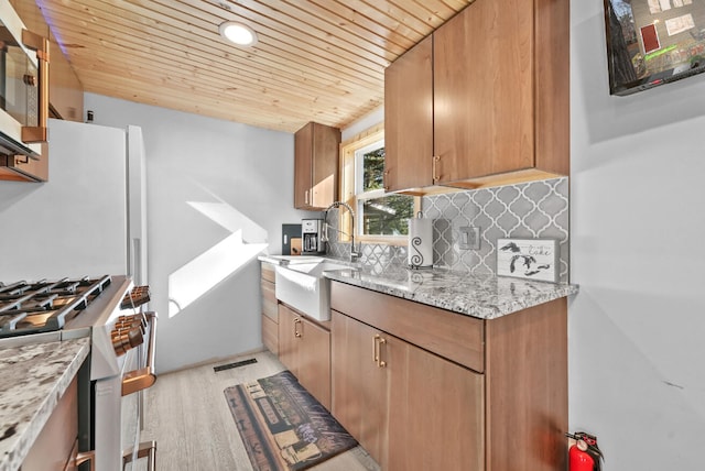 kitchen with stainless steel appliances, wood ceiling, sink, light stone countertops, and light hardwood / wood-style flooring