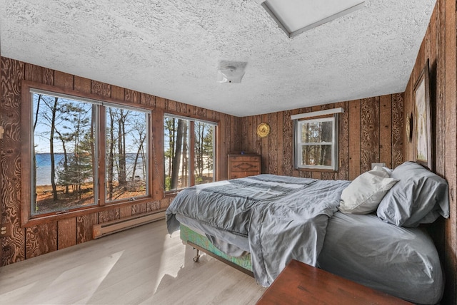 bedroom with a baseboard radiator, a water view, a textured ceiling, wooden walls, and light wood-type flooring