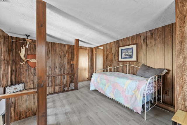 bedroom featuring hardwood / wood-style floors, wooden walls, and a textured ceiling