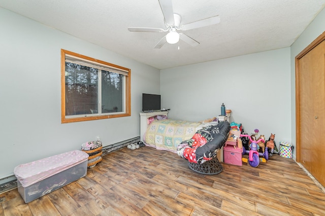 bedroom with a textured ceiling, a baseboard heating unit, ceiling fan, and hardwood / wood-style flooring